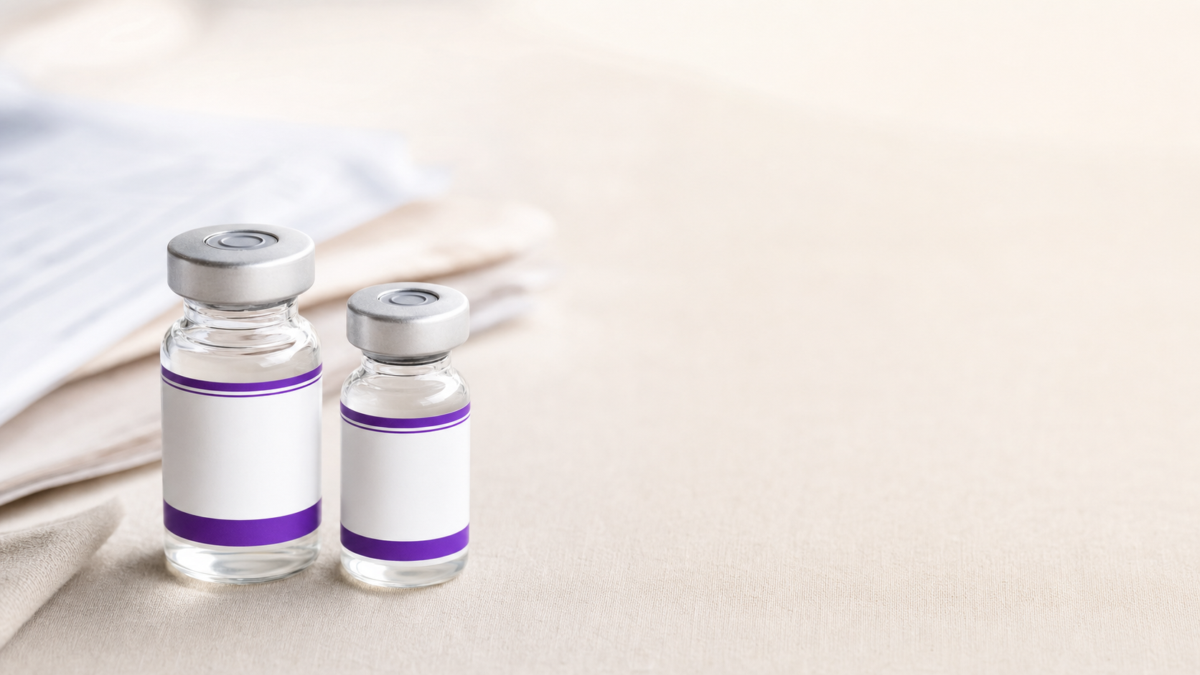 Two small clear glass medication vials with blank white and purple labels sitting on a light neutral surface.