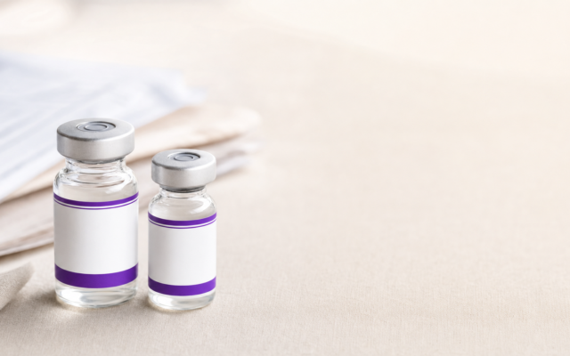 Two small clear glass medication vials with blank white and purple labels sitting on a light neutral surface.